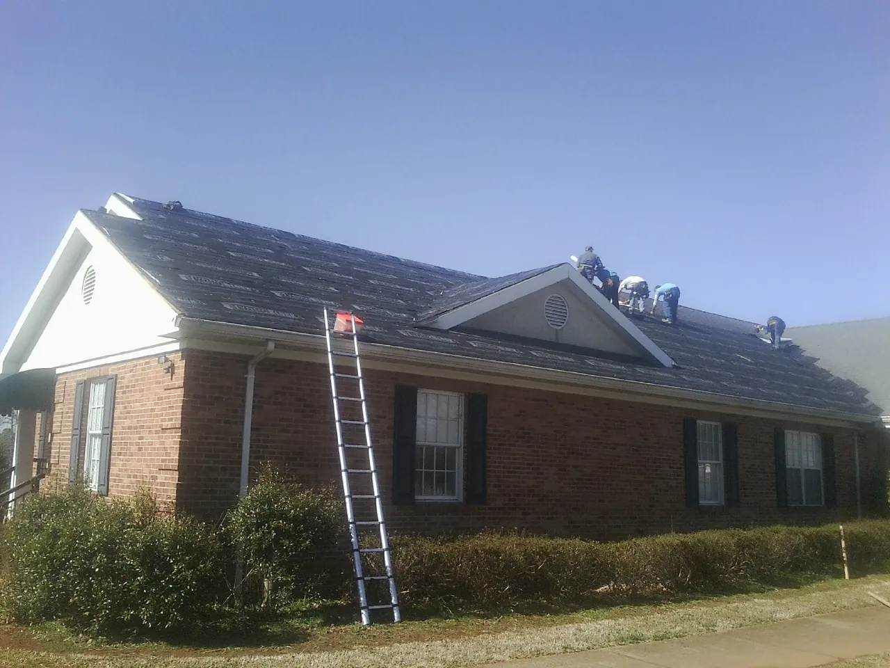 Crew tearing shingles off a brick ranch roof with a ladder set — Emergency Roof Repair work by our crew in River Forest