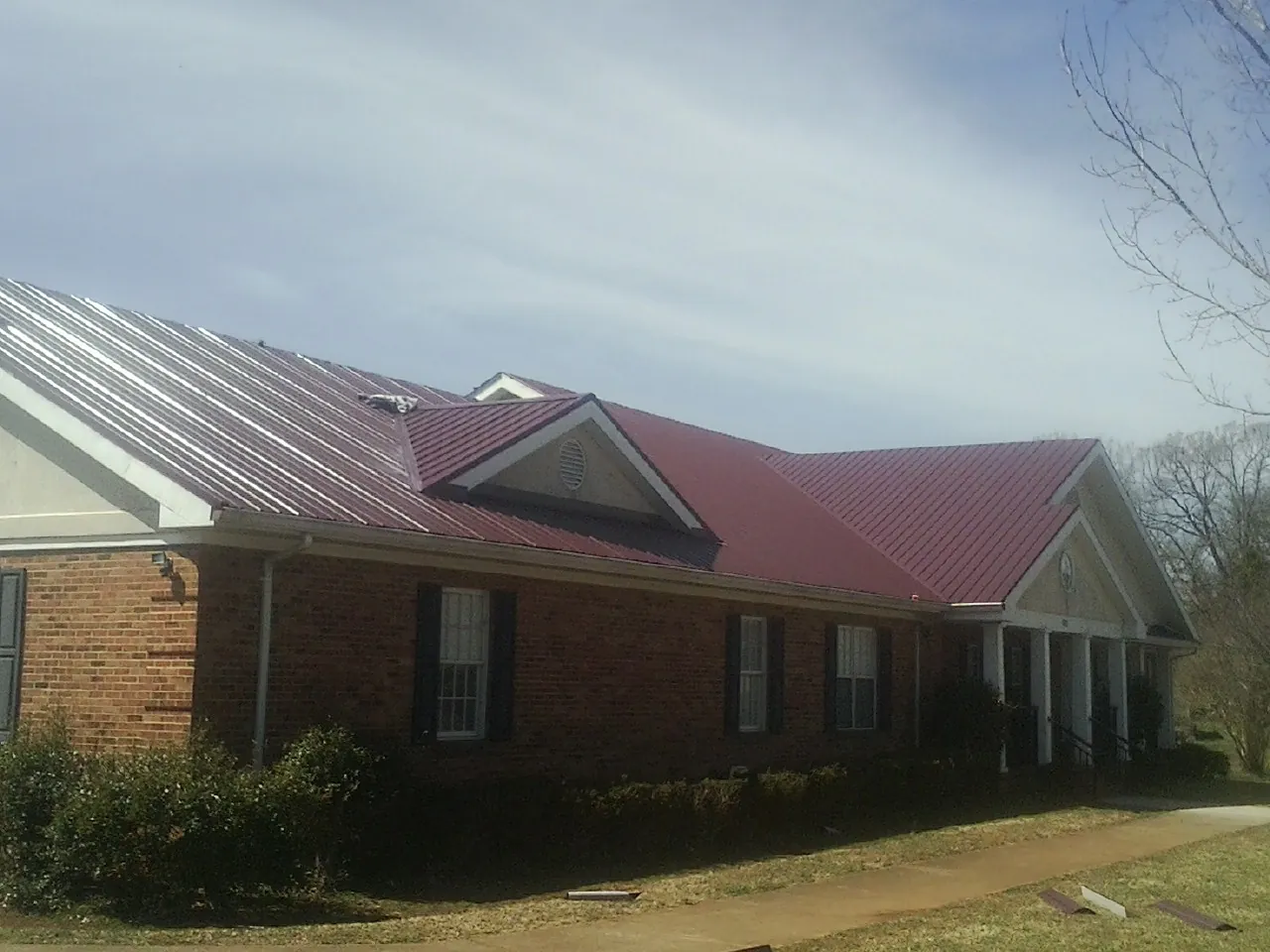 Red metal roof with gabled entries on a long brick building, from a Hail Damage Roof Repair job in River Forest