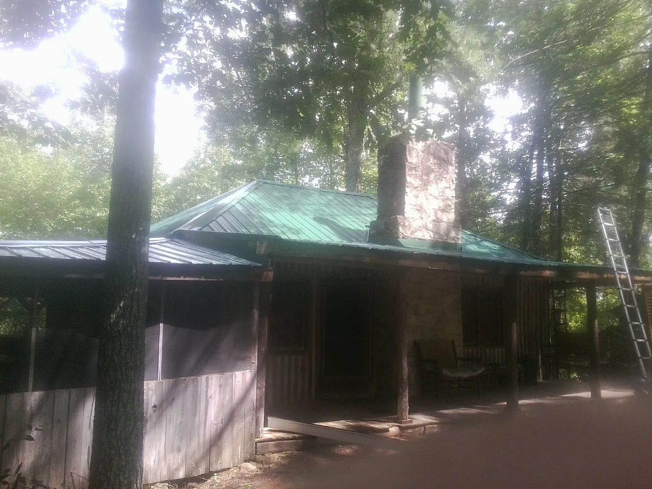 Green metal roof and stone chimney above a log cabin porch in River Forest