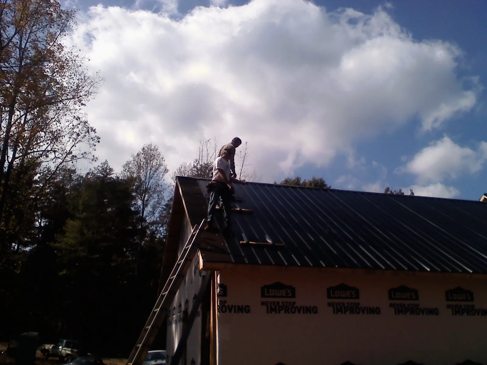 Roofer fastening dark metal panels high against a cloudy sky, from a Roof Inspection job in River Forest